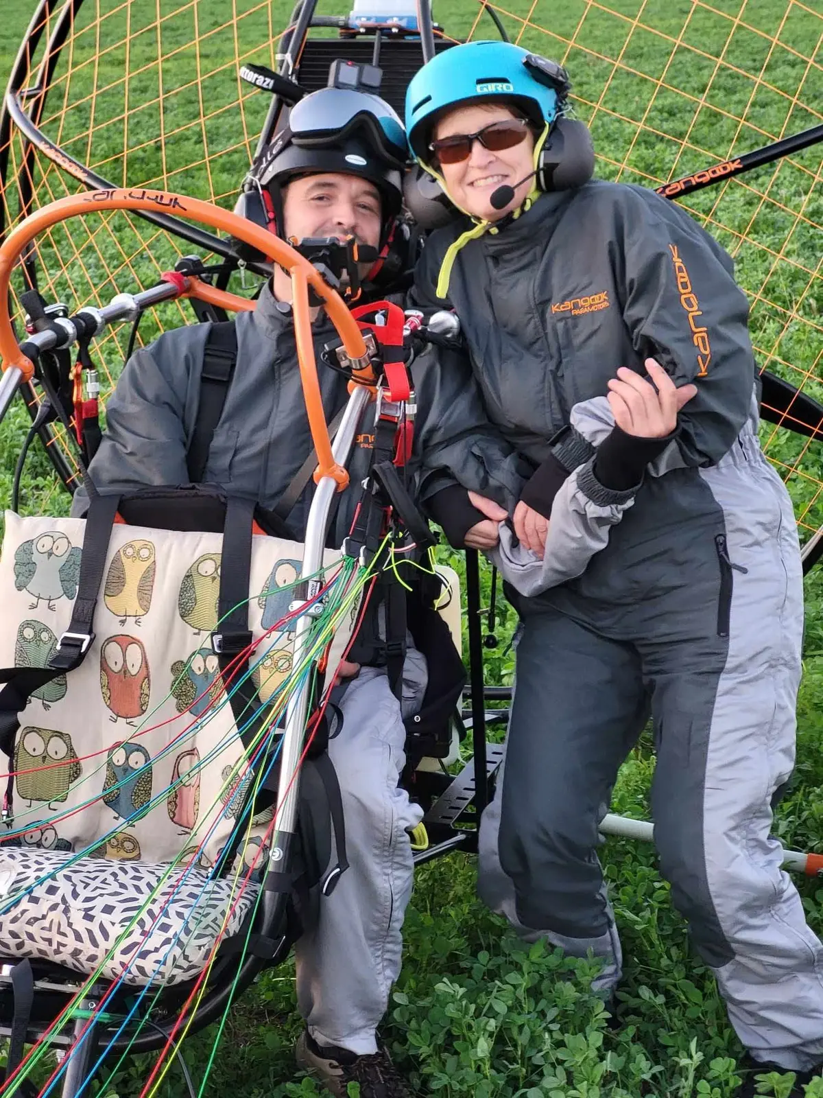 Deux pilotes souriants dans le paramoteur, casque bleu, au coucher du soleil